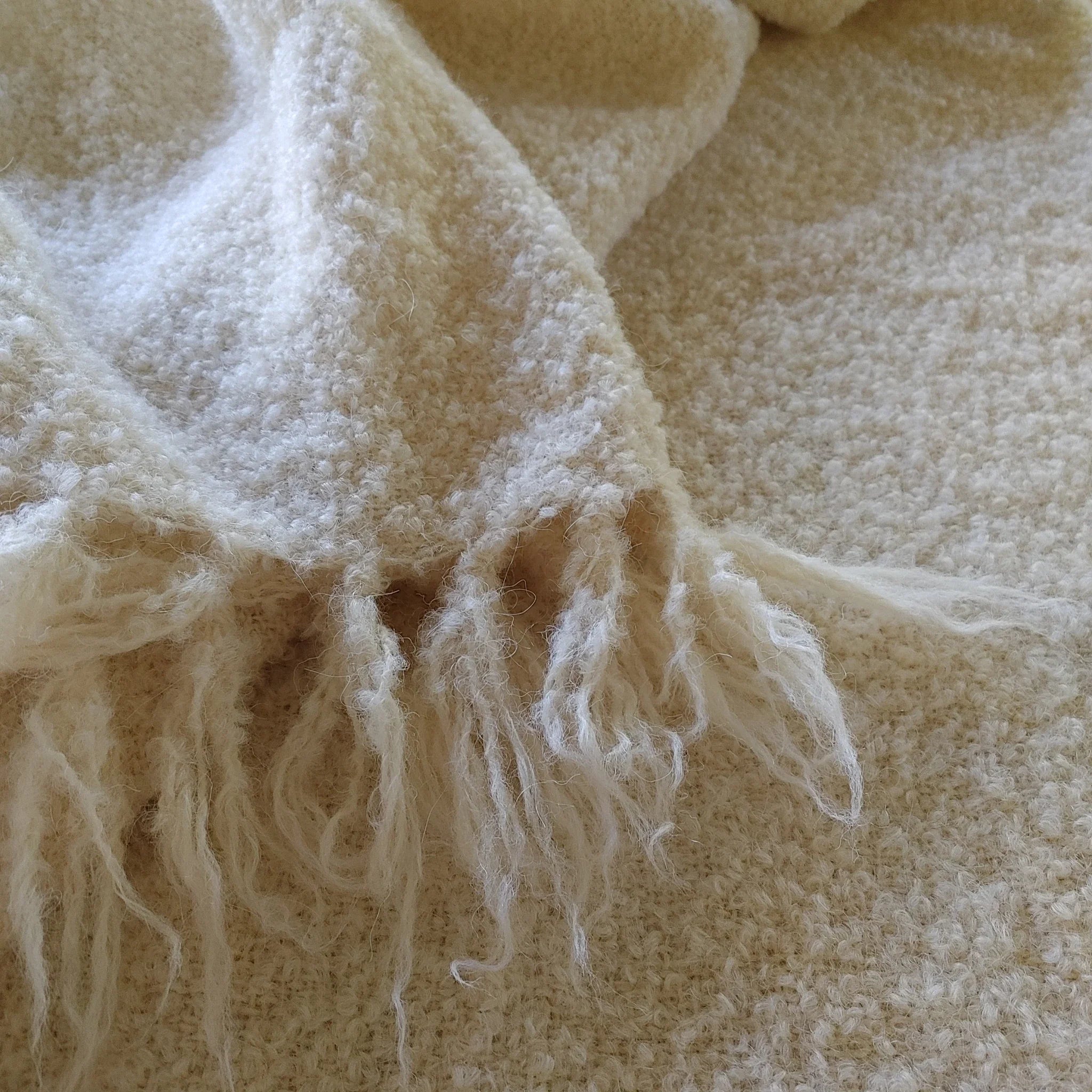 Folded corner of natural white alpaca loop yarn throw showing boucle texture and fringe