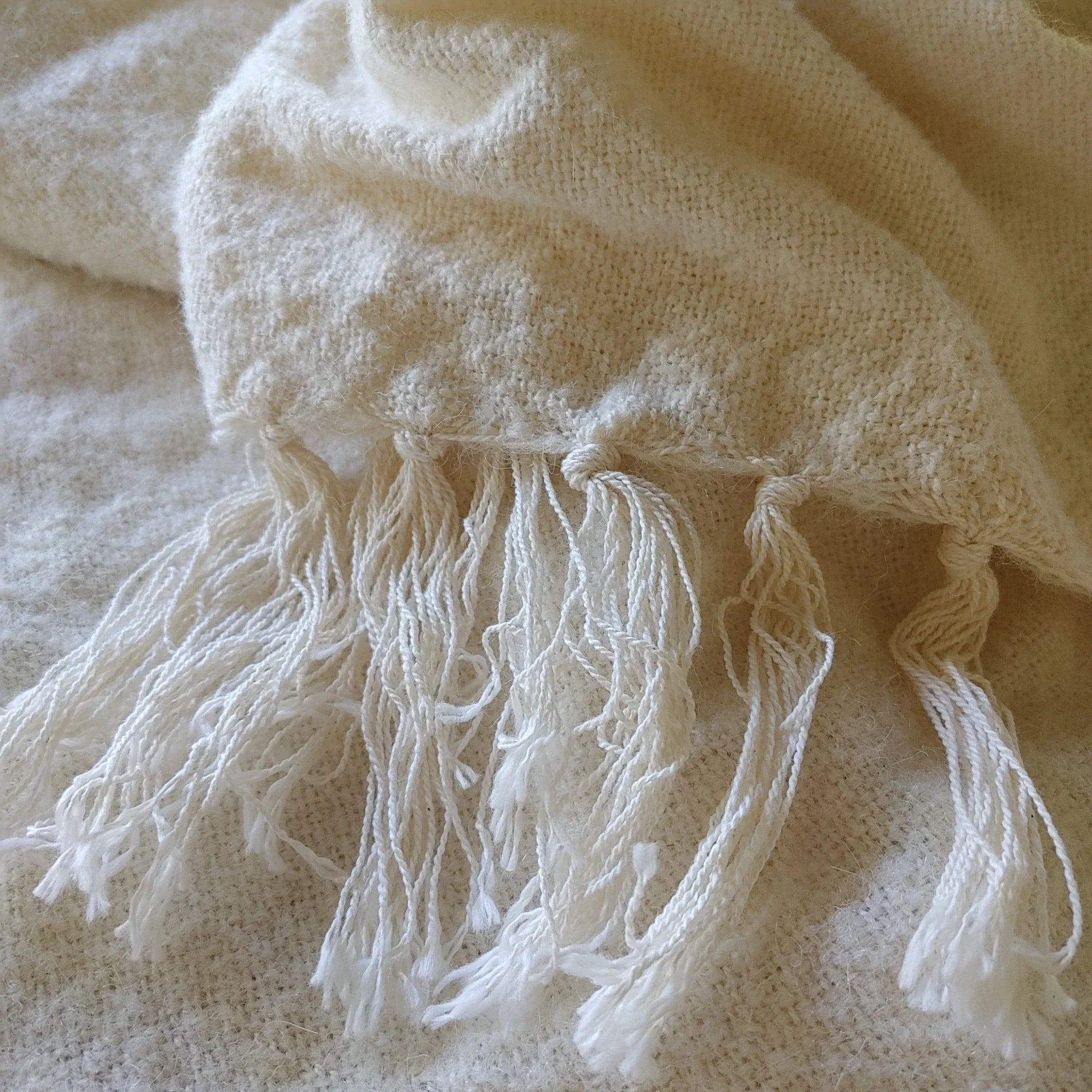 Folded corner of natural white alpaca silk throw showing flat weave texture and fringe